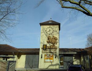 Eingangsbereich. Treppenaufgang mit Handlauf. Ein Gebäude mit einem Turm. Die Eingangstüren sind verschlossen.