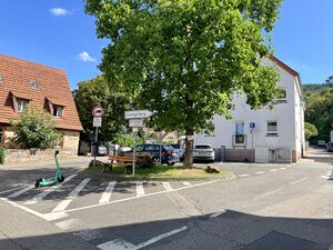 Zwei Straßen gabeln sich V-förmig. Im V ein kleiner Platz mit einem Baum und einer Sitzbank.